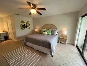 A bedroom with a bed, a ceiling fan, a nightstand, a lamp, a painting, and a view through a glass door. - 3BR Marco Island home with heated pool, WiFi, and full kitchen (Marco Island)
