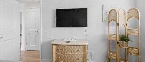 A room with a television mounted on the wall, a wicker side table, a rattan chair, and a bed.