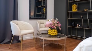 Una habitación moderna con dos sillas blancas, una mesa redonda con un florero y un espejo, además de una estantería oscura.