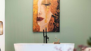 Un baño moderno con una bañera independiente, una obra de arte en la pared y una copa de vino al lado.