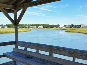 A wooden deck with a bench overlooking a calm body of water, surrounded by houses and greenery.