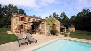 A stone house with a swimming pool, outdoor seating, and a garden.
