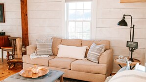 Ein gemütliches Wohnzimmer mit einem beigefarbenen Sofa, einem kleinen Holztisch mit Tablett, einer Lampe und einem Sessel.