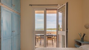 A bedroom with a bed, a wardrobe, a sliding glass door leading to a balcony with a table and chairs, and a nightstand with a lamp. - Residence a Marinella a 450 mt dal mare  (Golfo Aranci)