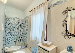A bathroom with a mosaic tile shower, a white toilet, a sink, and a mirror with a decorative frame. - Residence a Marinella a 450 mt dal mare  (Golfo Aranci)