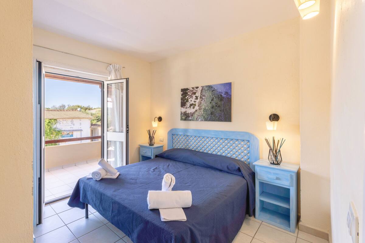 Een slaapkamer met een bed, twee nachtkastjes, een raam en een schilderij aan de muur.