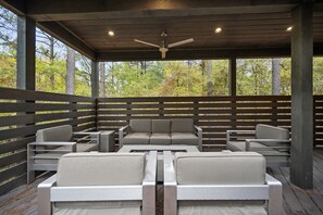 Relax in this serene outdoor seating area, complete with a ceiling fan and comfortable seating for guests to enjoy the surrounding forest views.