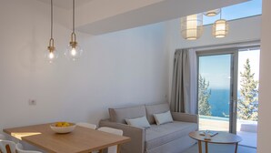 A modern living room with a sofa, dining table, and chairs. There is a view of the ocean through the window. - Brand New Villa Ionion Theasis Armonia with sea view & private pool (Lefkada)