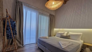 A bedroom with a large bed, a wooden floor, a hanging light fixture, and a window with curtains.