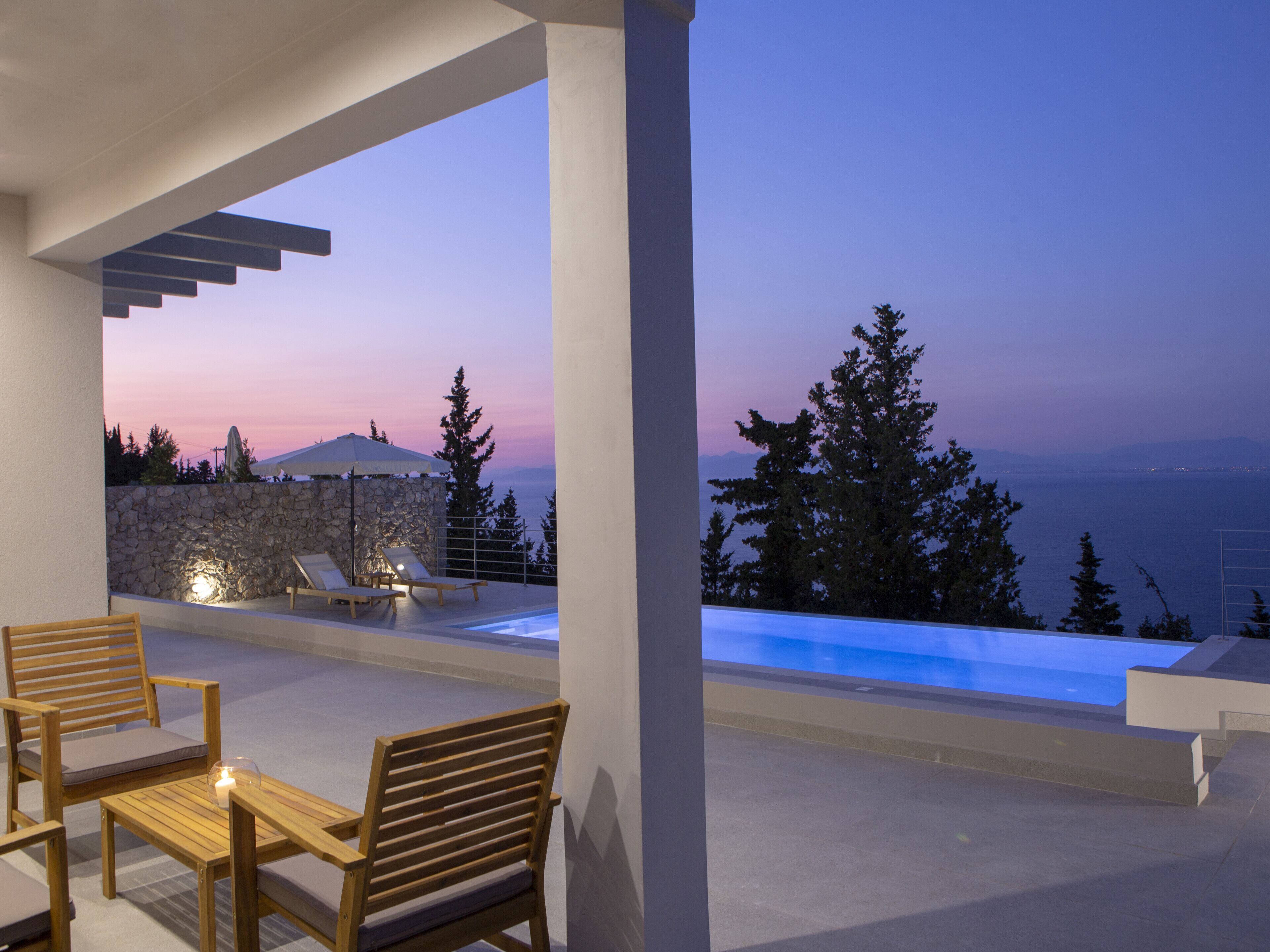 Un área de estar moderna al aire libre con piscina y vista al mar al atardecer.