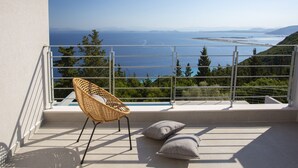A balcony with a wicker chair and cushions, overlooking a scenic view of the sea and hills.