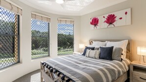 A bedroom with a large bed, a nightstand, a lamp, and a painting of flowers on the wall. - The Sails - 2-21 Beech Street (Evans Head)