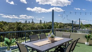 An outdoor terrace with a table and chairs, surrounded by greenery and a clear sky. - The Sails - 2-21 Beech Street (Evans Head)