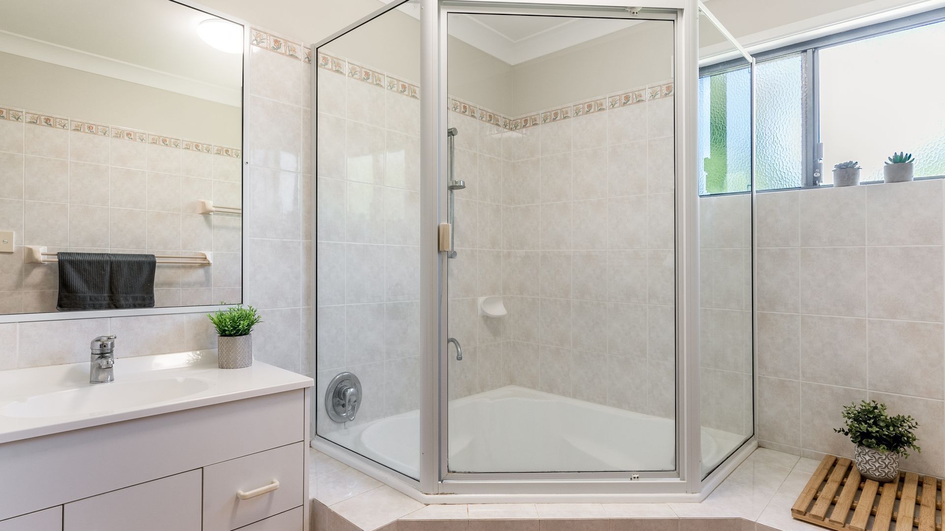 Une salle de bain moderne avec une douche à parois de verre, un meuble-lavabo blanc et une petite plante en pot.