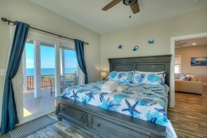 Quarto com cama, cortinas, ventilador de teto e vista para o oceano.