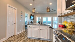 A modern kitchen with a central island, white cabinetry, stainless steel appliances, and pendant lighting. - Oceanfront | Private Pool & Hot Tub | Adventures in Paradise (Oak Island)