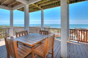Área externa coberta com mesa e cadeiras de madeira, com vista para a praia.