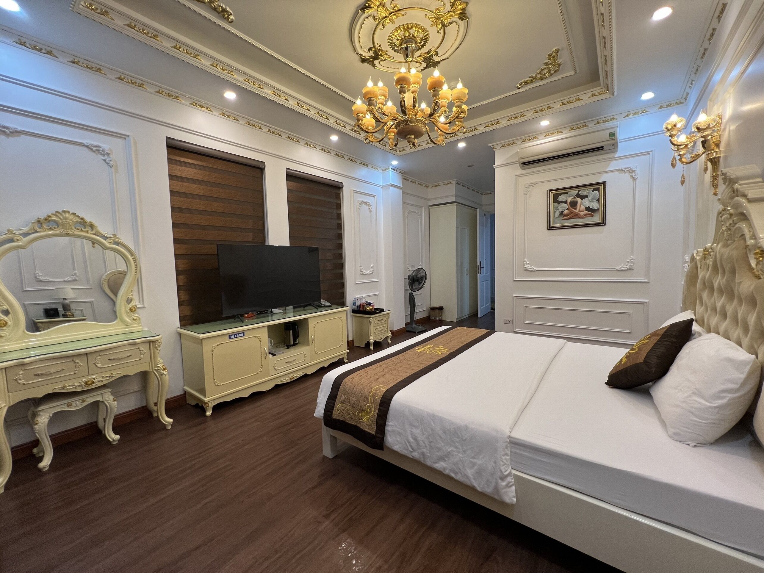 A bedroom with a large bed, a television on a cabinet, and a chandelier.