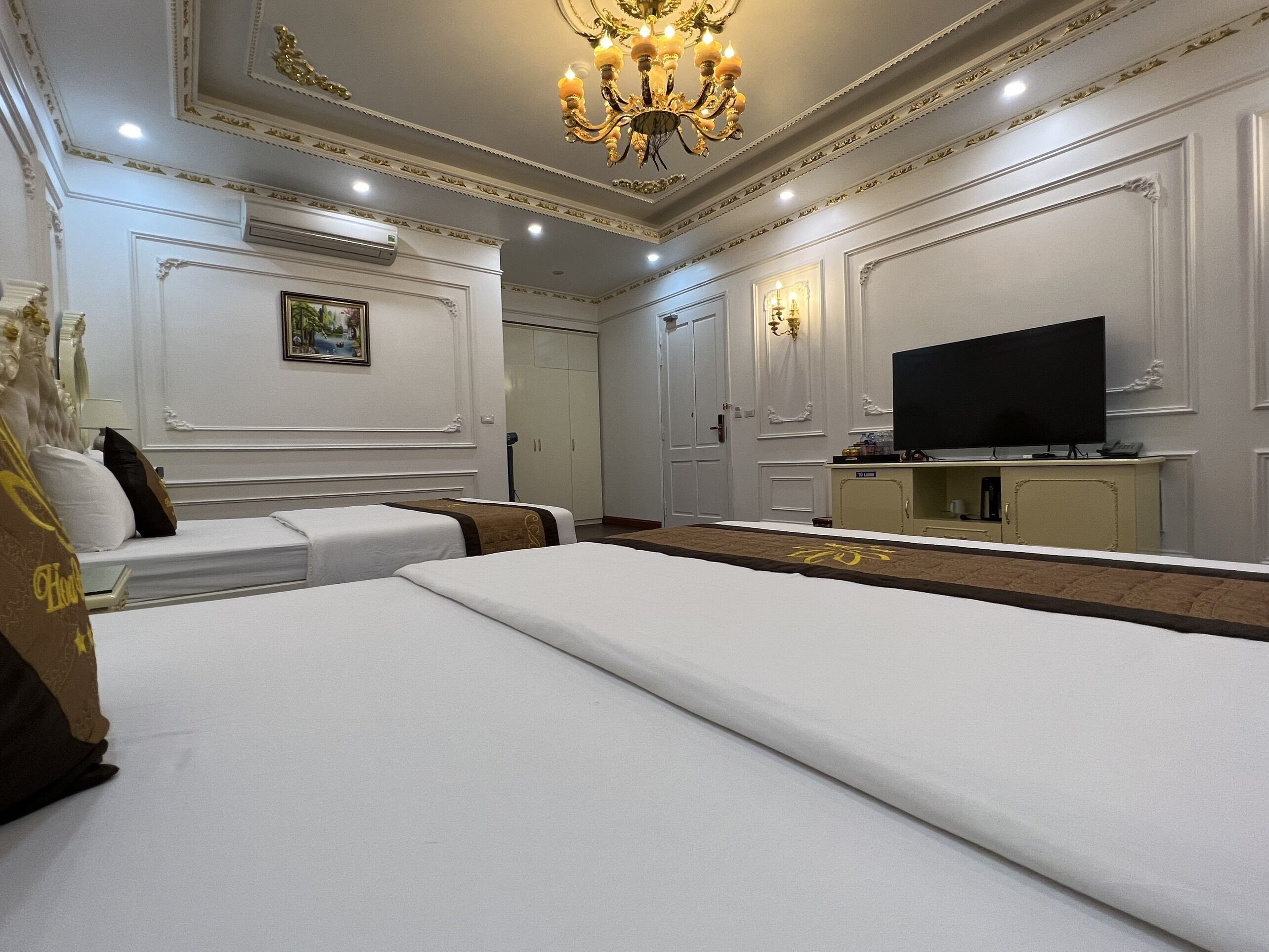 A hotel room with two beds, a television, and a chandelier.