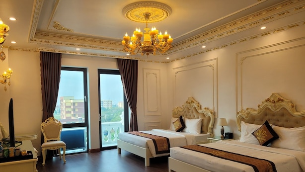 A hotel room with two beds, a chandelier, and a view of the city. - Hoa Dong Aureum Hotel Ha Nam (Phu Van)