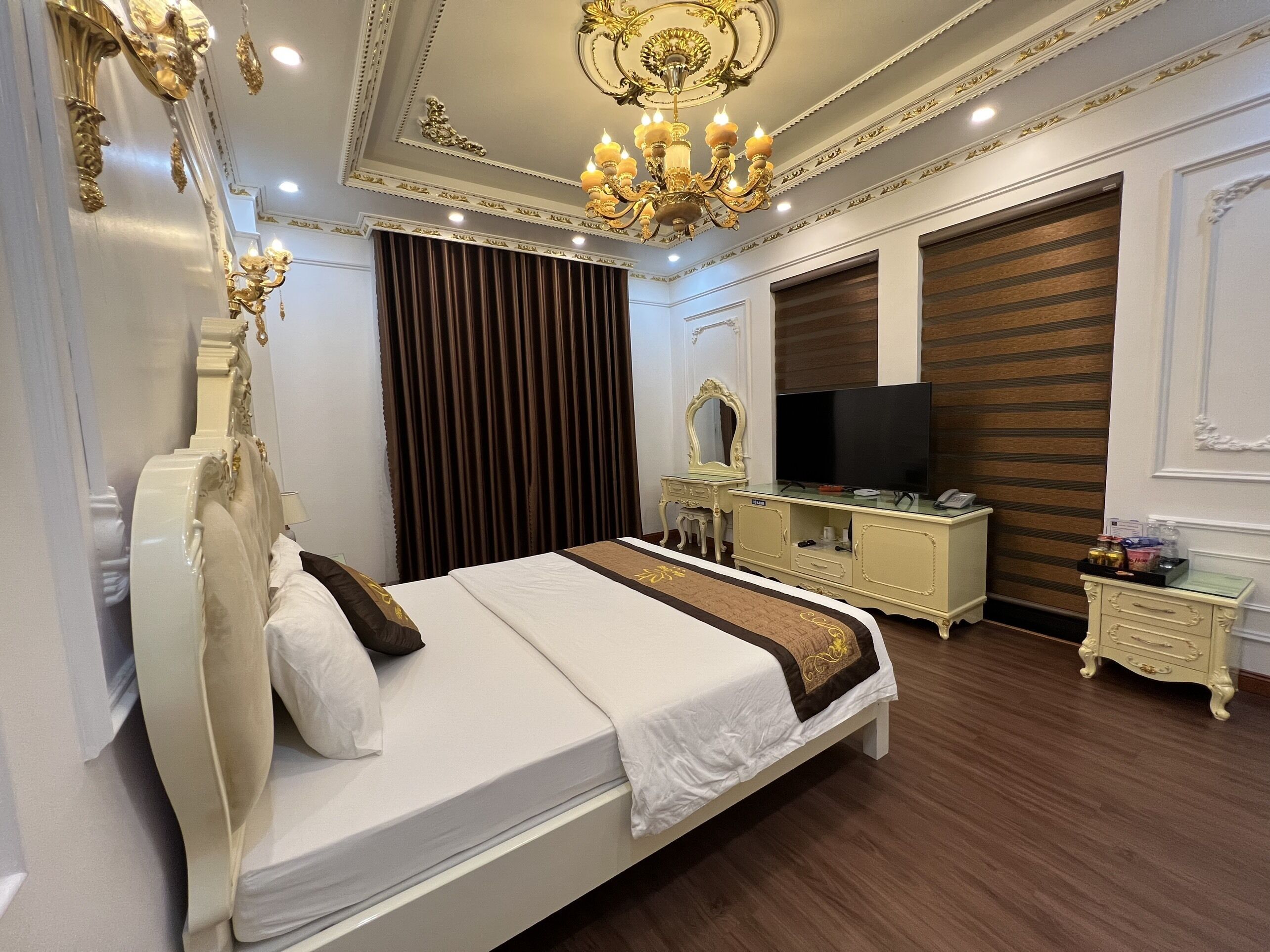 Une chambre d’hôtel élégamment aménagée, dotée d’un grand lit, d’une télévision, d’une coiffeuse avec un miroir et d’un lustre.