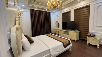 Une chambre d’hôtel élégamment aménagée, dotée d’un grand lit, d’une télévision, d’une coiffeuse avec un miroir et d’un lustre.