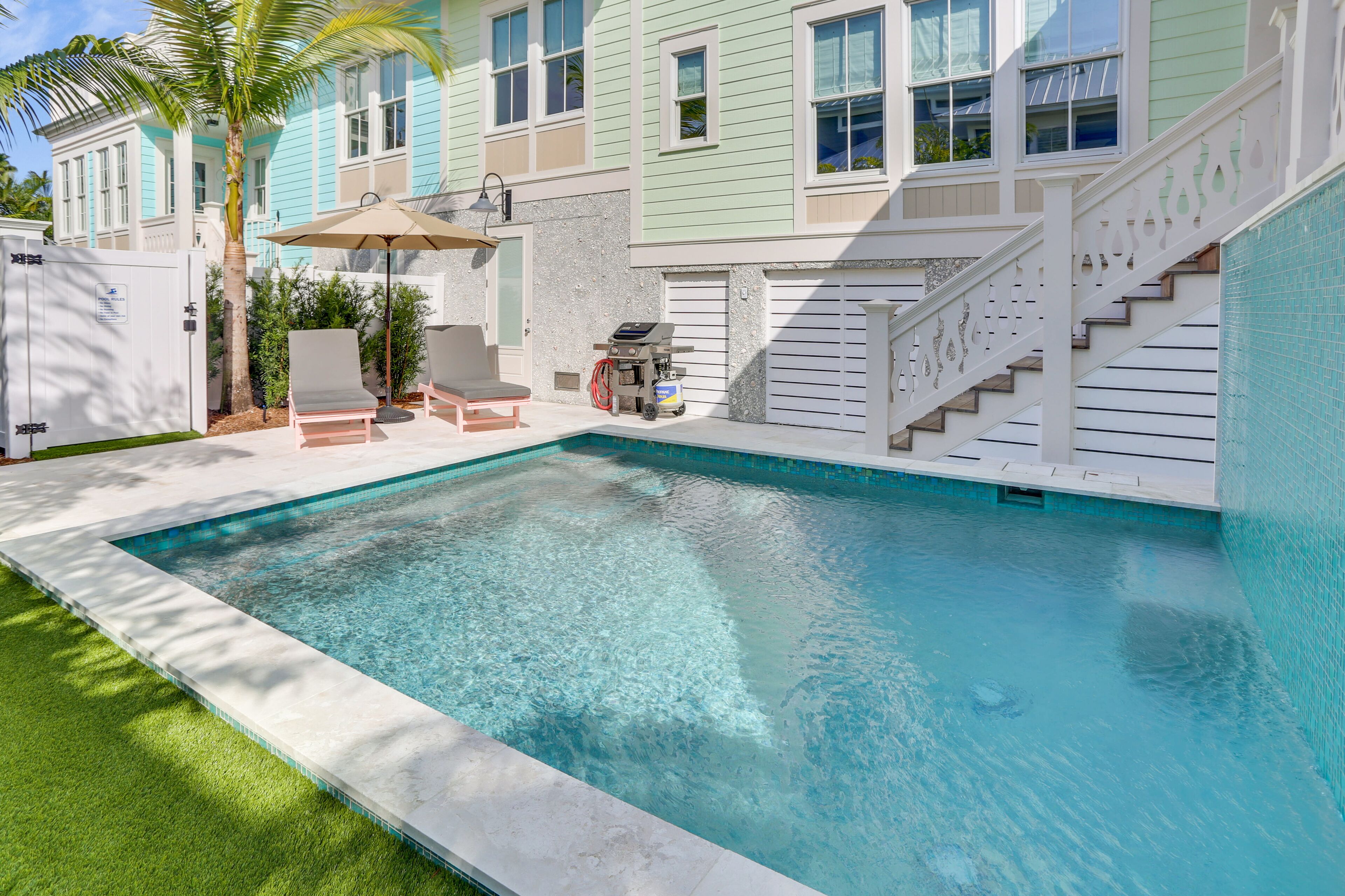 A swimming pool with a white deck, a covered patio area, and a staircase leading to a garage.