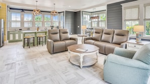 Ein geräumiges Wohnzimmer mit einem beigefarbenen Ecksofa, einem runden Couchtisch und einem Essbereich mit einer grönen Kücheninsel.
