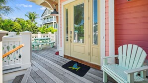 Una terraza de madera con una puerta, un sillón Adirondack verde y una mesa de picnic.