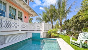 Una piscina con solárium de baldosas, rodeada por una valla blanca con adornos decorativos y palmeras al fondo.