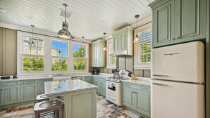 A kitchen with green cabinets, a white refrigerator, and a large window with blinds.