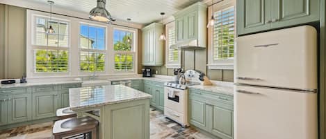 A kitchen with green cabinets, a white refrigerator, and a large window with blinds.