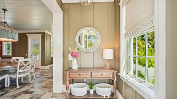 A well-lit hallway with a wooden console table, two white baskets, a mirror, and a window with a view of greenery.