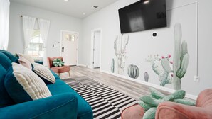 Una sala de estar moderna con un sofá azul turquesa, un tapete a rayas negras y blancas y un mural temático de cactus.