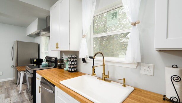 Una cocina moderna con armarios blancos, un refrigerador de acero inoxidable, una encimera de madera y un grifo dorado.