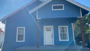 Una casa de dos pisos con fachada azul, una puerta blanca y dos ventanas en la planta baja.