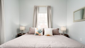 Un dormitorio con cama, dos lámparas de noche, una ventana con cortinas y un espejo en la pared.