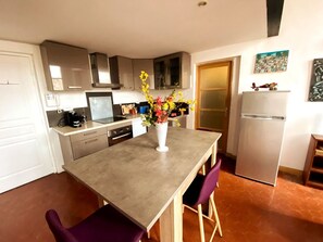 Une cuisine compacte comprenant une table à manger, des chaises, un réfrigérateur et un vase avec des fleurs.