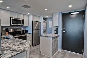 A modern kitchen with white cabinets, a stainless steel refrigerator, a microwave, and a coffee maker.