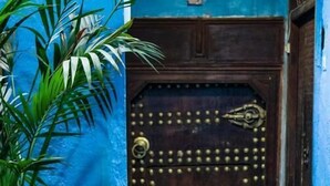 Une porte en bois ornée de clous et d’une poignée en laiton, le tout contrastant avec un mur bleu.