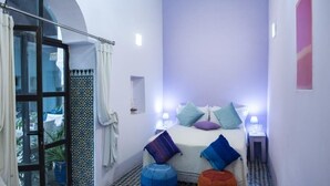 Une petite pièce comprenant un lit, deux tables de chevet, une fenêtre avec des rideaux et une porte.