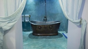 Une salle de bain avec une baignoire sur pieds d’époque, des rideaux blancs et un mur bleu.