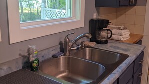 A kitchen with two stainless steel sinks, a window with a view of trees, and dark cabinets.