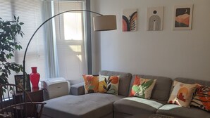 A living room with a sectional sofa, a round coffee table, a wooden chair, a floor lamp, and artwork on the wall.