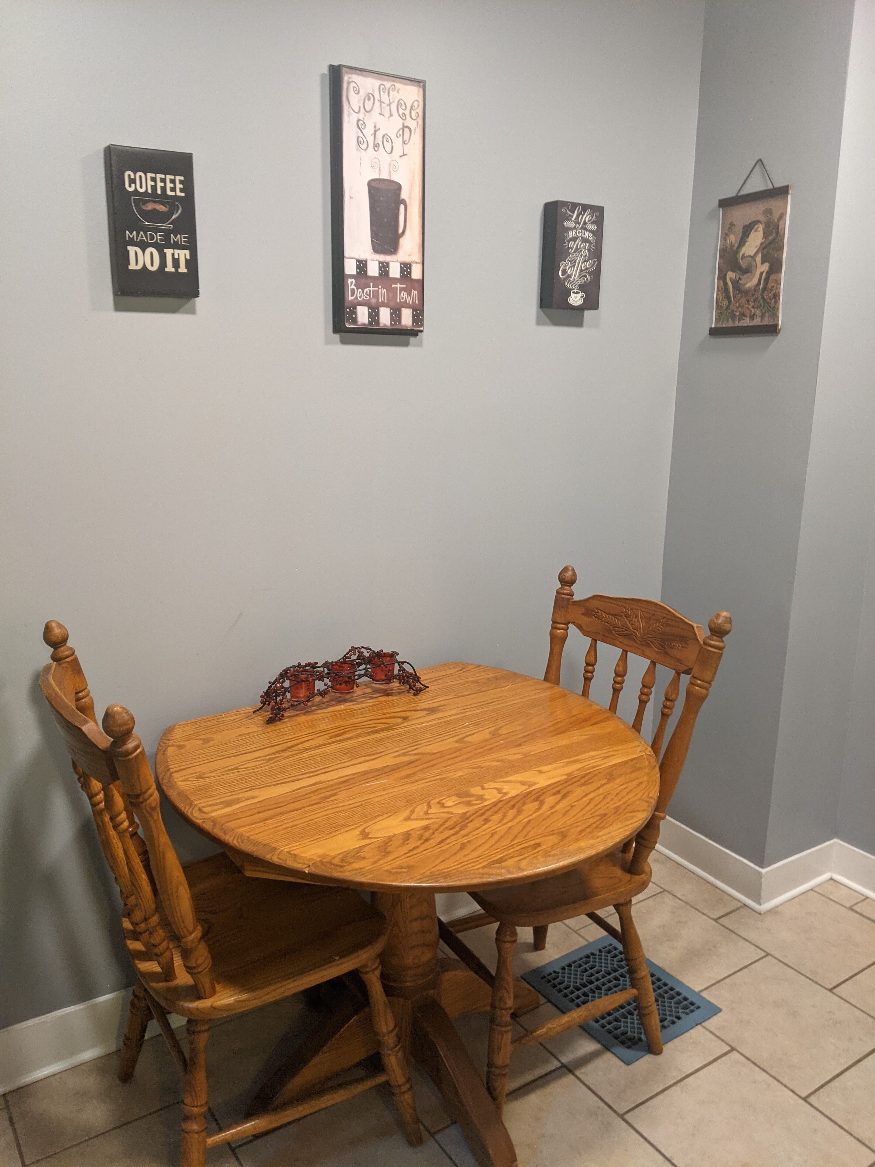 Una mesa de comedor de madera con dos sillas, una decoración de pared con temática de café y una obra de arte pequeña enmarcada.