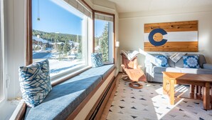 A cozy living area with a large window seat, a wooden table, and a view of a snowy landscape. - Amazing Copper Mountain Views, free wifi, free parking. (Copper Mountain)