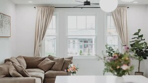 A modern living room with a beige sofa, a white coffee table, and a potted plant. - Modern Downtown Indy Apt - King Bed, Patio & Cute Flower Shop Below (Indianapolis)