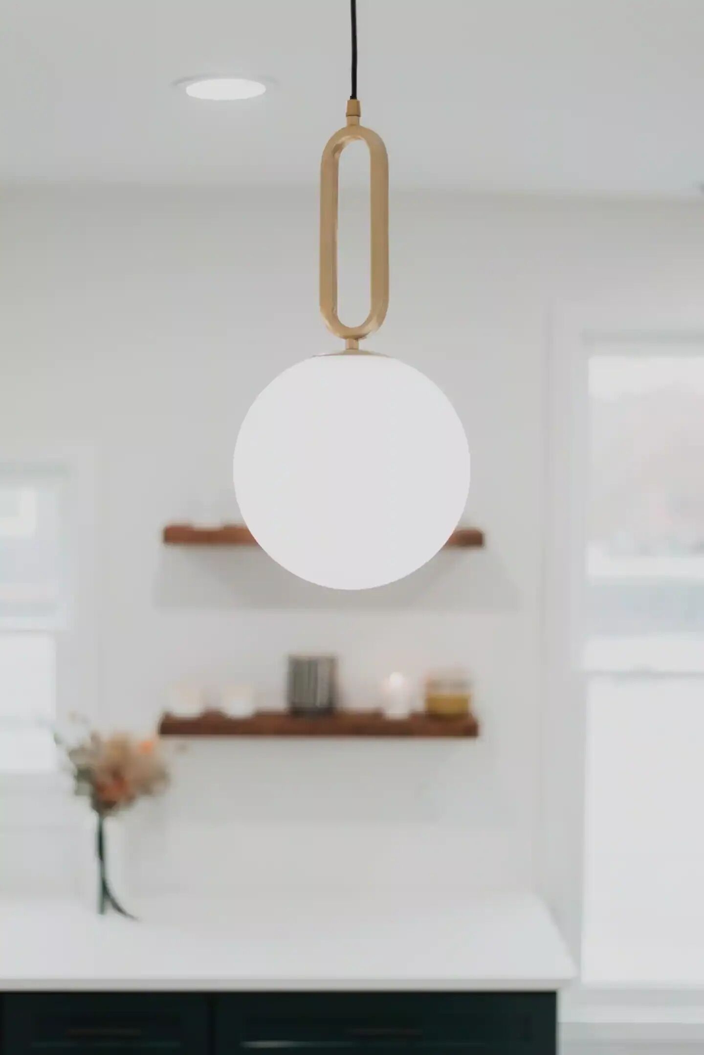 A modern kitchen with a white countertop, a hanging pendant light, and a wooden shelf with decorative items.