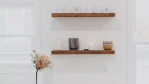A white wall with two wooden shelves, a white vase with dried flowers, and a green cabinet below. - Modern Downtown Indy Apt - King Bed, Patio & Cute Flower Shop Below (Indianapolis)