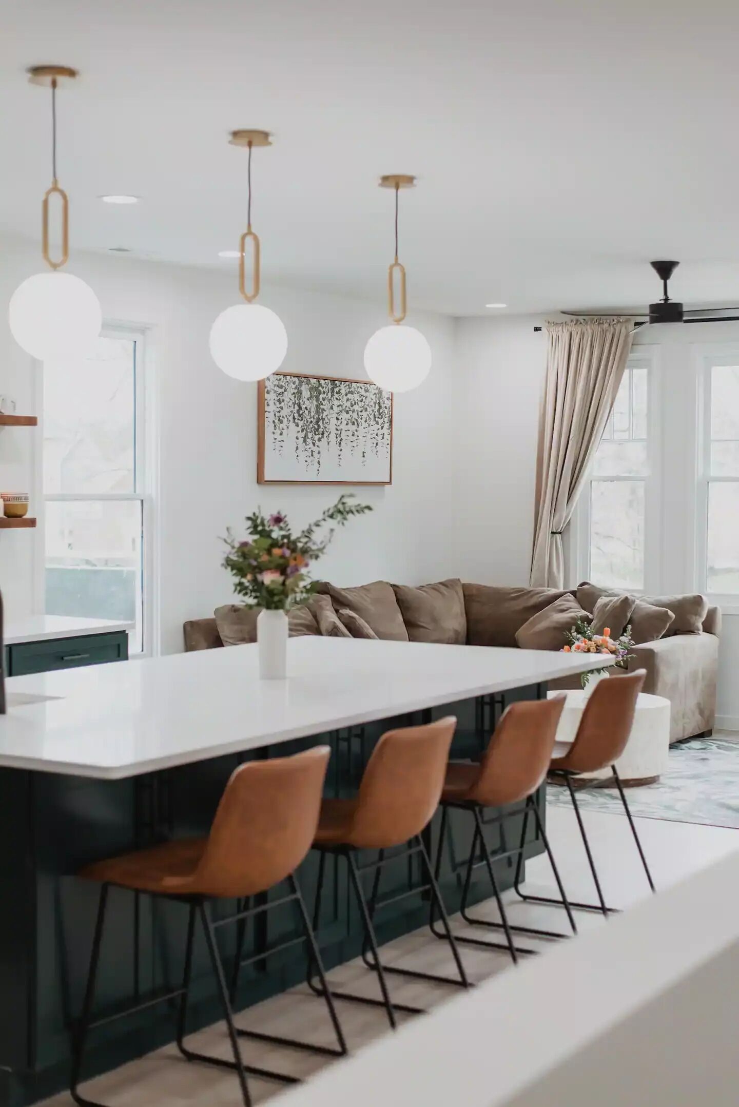 A modern kitchen with a central island, pendant lights, and a dining area with chairs.